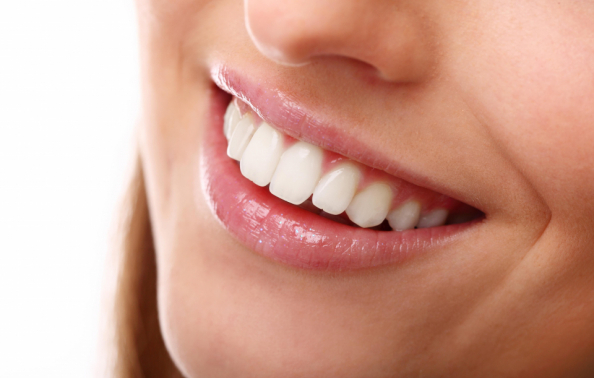 Zbliżenie na uśmiechnięte usta kobiety z czystymi i równymi zębami.